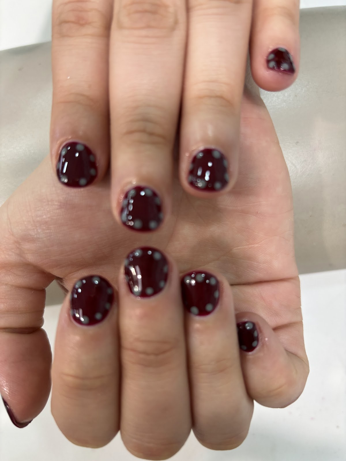 Ongles courts bordeaux foncé, à pois blancs peints à la main.